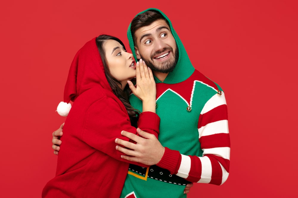 Couple wearing matching custom Christmas hoodies, laughing and celebrating