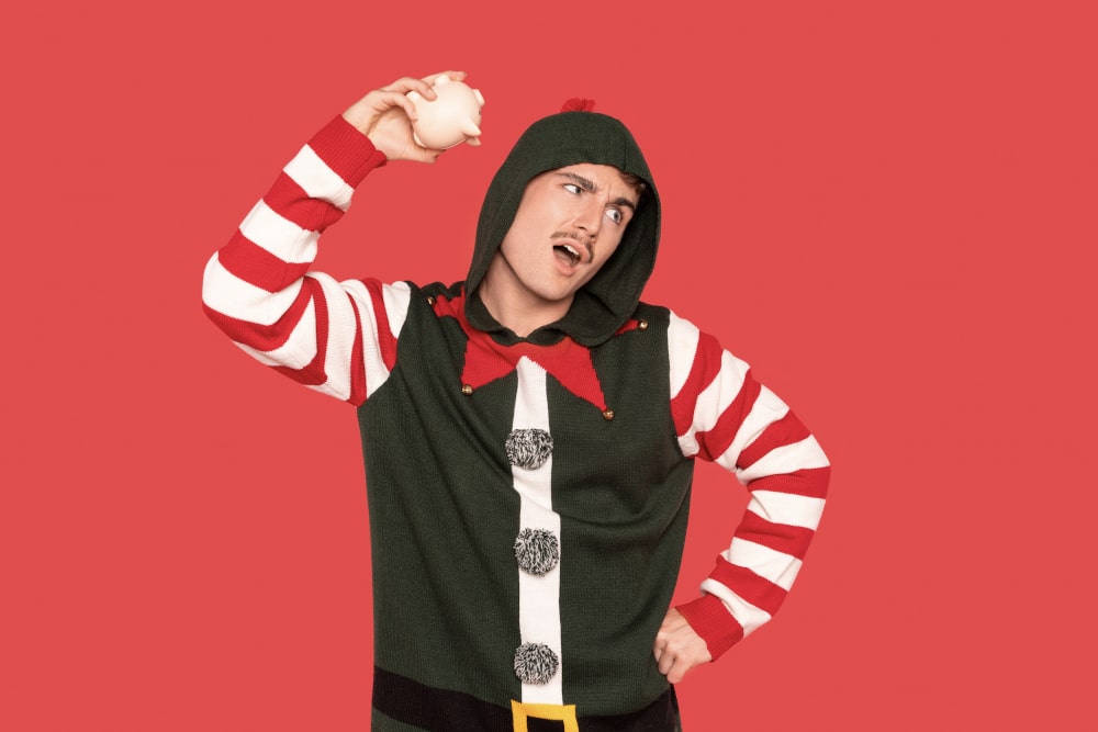 Person dressed as cheerful elf in holiday hoodie throwing snowball