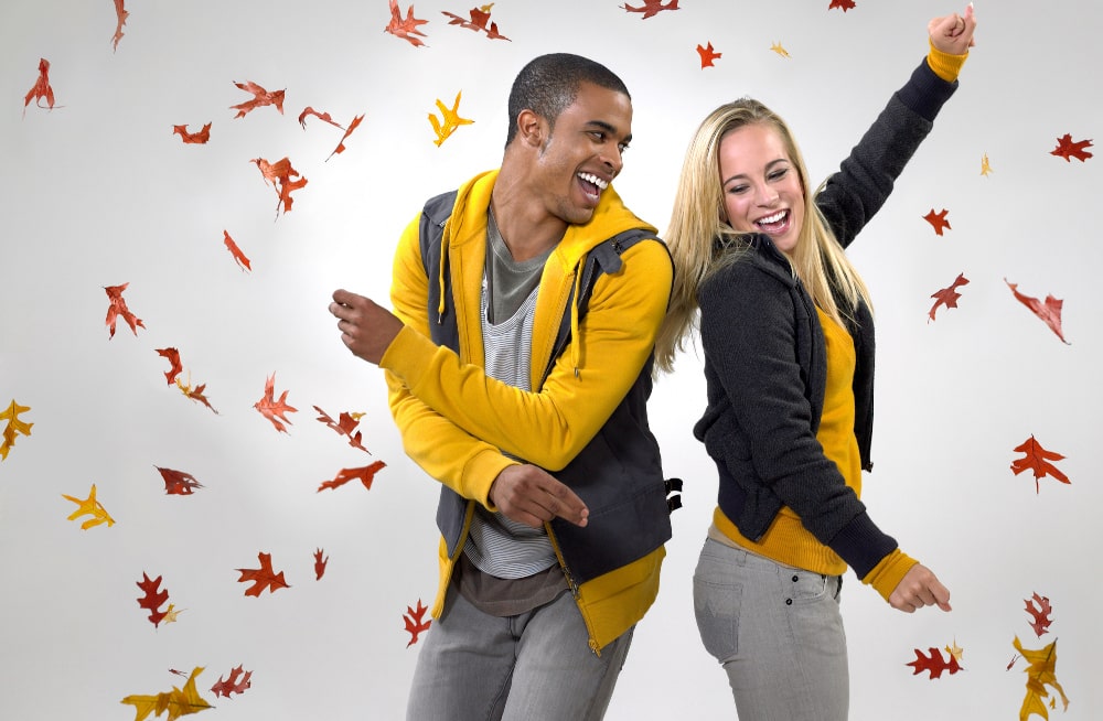 Young couple wearing custom fall apparel while dancing in leaves in Toronto